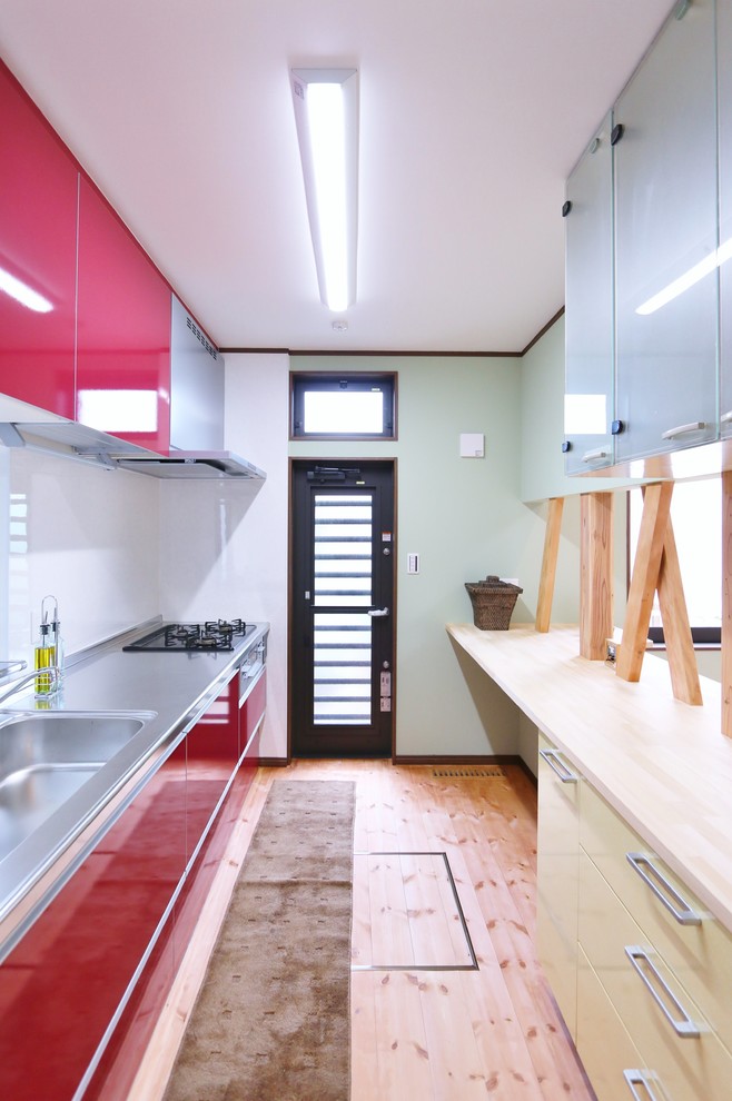 Inredning av ett modernt beige linjärt beige kök, med en integrerad diskho, släta luckor, röda skåp, ljust trägolv, en halv köksö och brunt golv