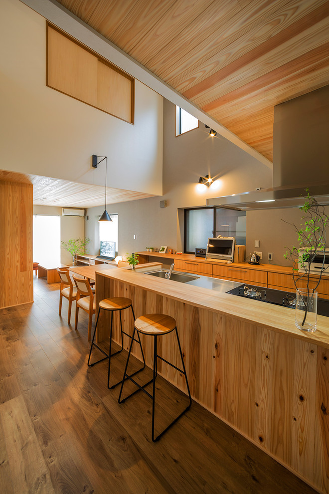 Bild på ett lantligt brun brunt kök med öppen planlösning, med släta luckor, skåp i mellenmörkt trä, bänkskiva i rostfritt stål, mörkt trägolv, en halv köksö, brunt golv och en enkel diskho
