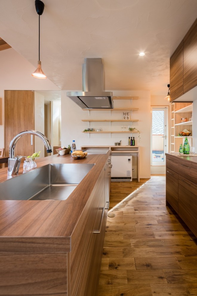 Example of a zen galley medium tone wood floor and brown floor open concept kitchen design in Other with a single-bowl sink, flat-panel cabinets, medium tone wood cabinets, wood countertops and an island