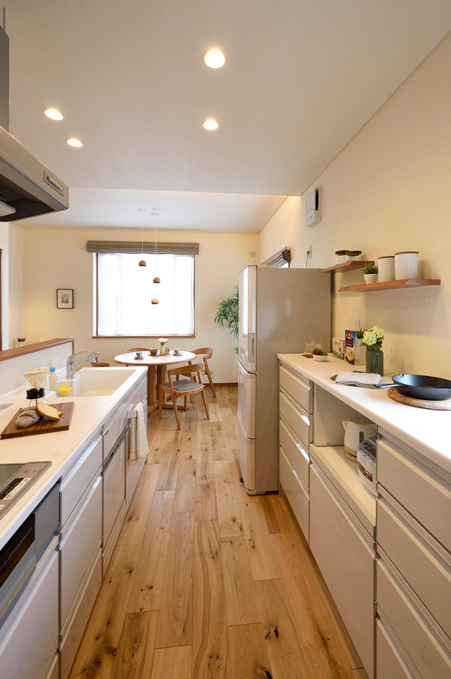 Modern inredning av ett mellanstort vit linjärt vitt kök, med en integrerad diskho, vita skåp, bänkskiva i koppar, vitt stänkskydd, glaspanel som stänkskydd, mellanmörkt trägolv, släta luckor, en halv köksö och brunt golv