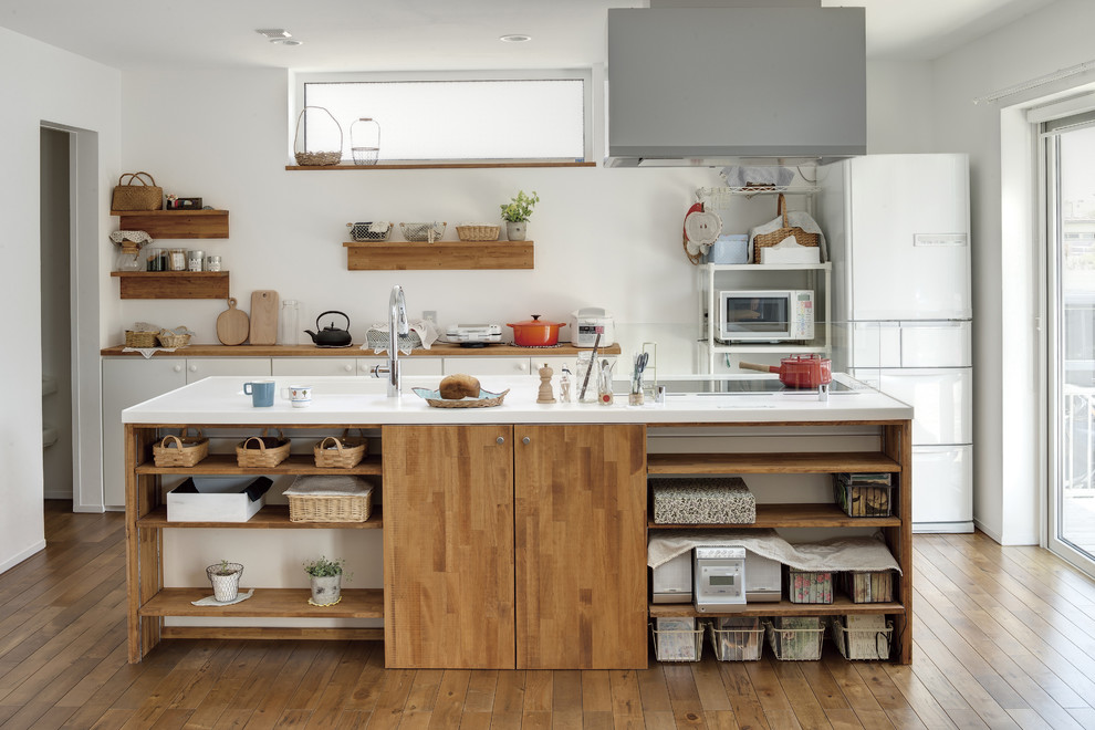 Zweizeilige Landhausstil Küche mit integriertem Waschbecken, offenen Schränken, hellbraunen Holzschränken, Küchenrückwand in Weiß, weißen Elektrogeräten, braunem Holzboden und Kücheninsel in Sonstige
