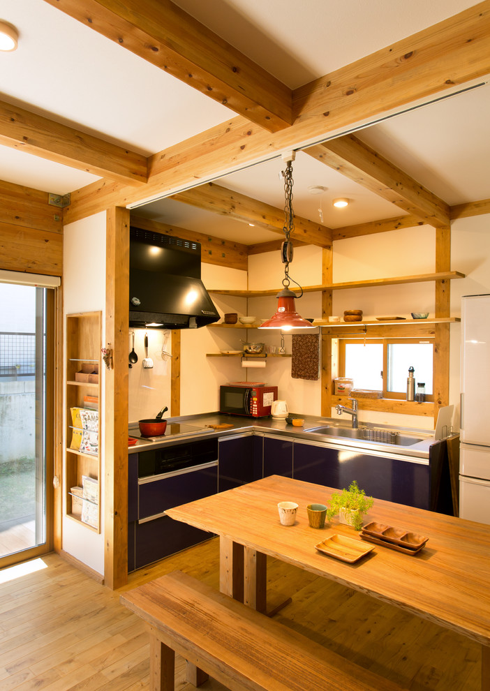 Cette image montre une cuisine ouverte asiatique en L avec un évier intégré, un placard à porte plane, des portes de placard noires, un sol en bois brun, une péninsule et un sol marron.