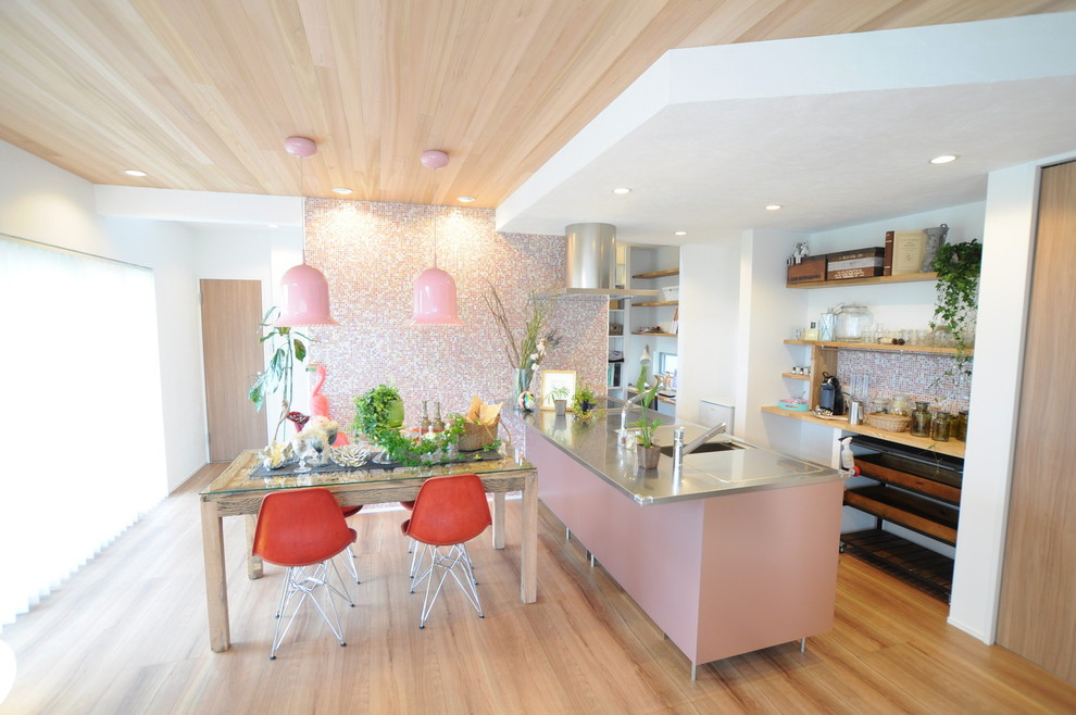 Идея дизайна: прямая кухня-гостиная в стиле лофт с монолитной мойкой, столешницей из нержавеющей стали, розовым фартуком, черной техникой, полуостровом и коричневым полом