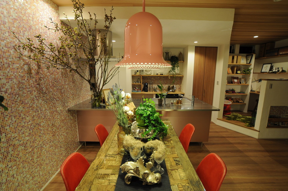 Cette photo montre une cuisine ouverte linéaire industrielle avec un évier intégré, un plan de travail en inox, une crédence rose, un électroménager noir, une péninsule et un sol marron.