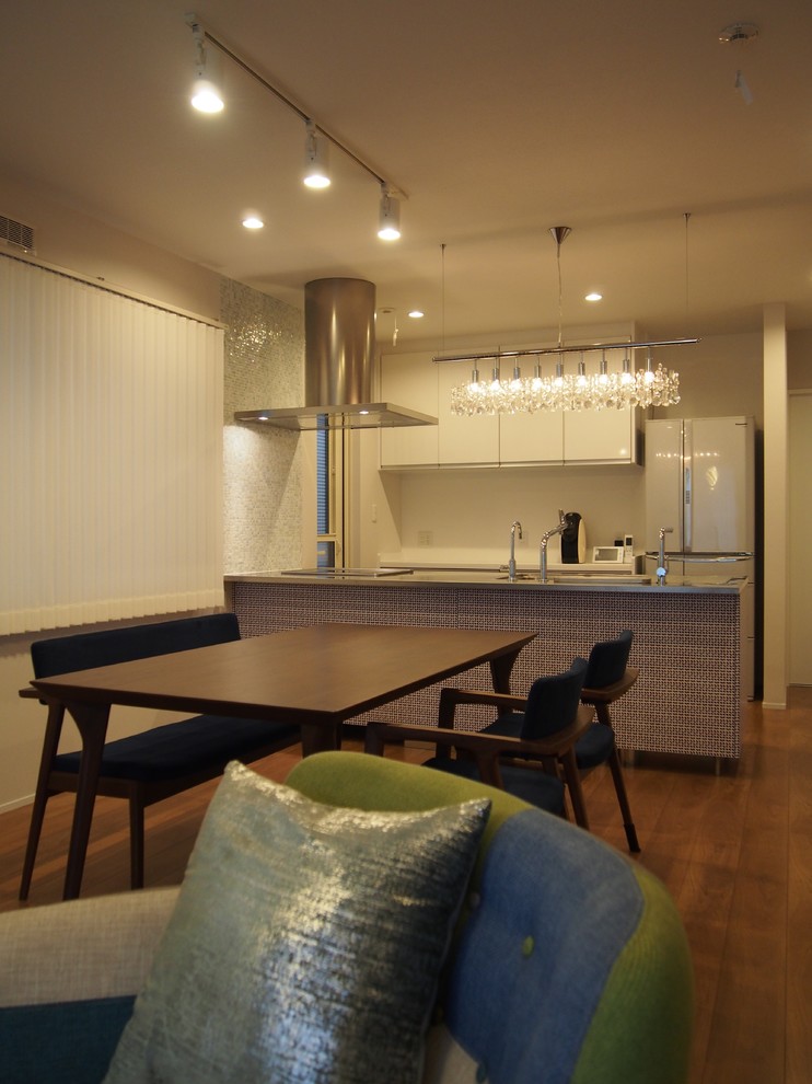 Example of a small minimalist single-wall light wood floor and brown floor open concept kitchen design in Tokyo with an integrated sink, blue cabinets, stainless steel countertops, blue backsplash, black appliances, an island and gray countertops