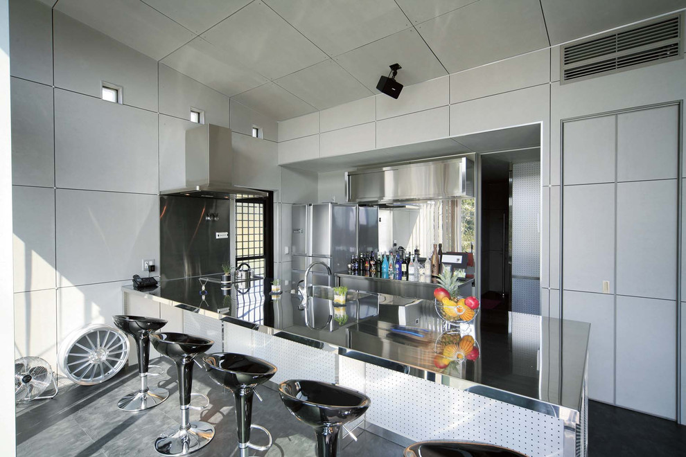 他の地域にあるコンテンポラリースタイルのおしゃれなキッチン (一体型シンク、フラットパネル扉のキャビネット、ステンレスカウンター、グレーの床) の写真