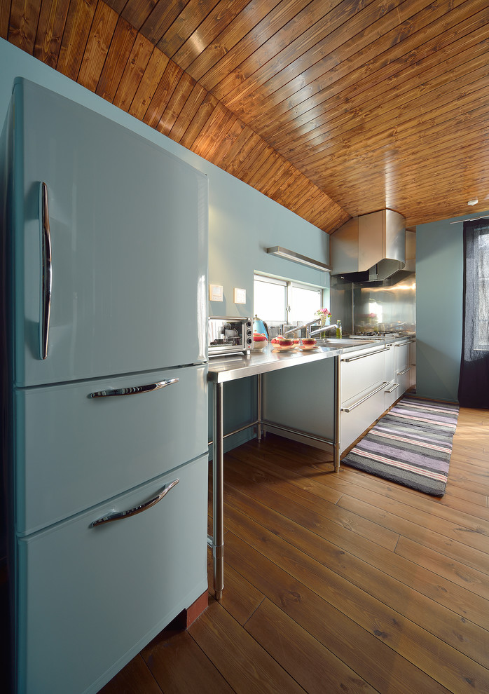 Modelo de cocina lineal bohemia con armarios con paneles lisos, puertas de armario blancas, encimera de acero inoxidable, salpicadero azul, suelo de madera en tonos medios y suelo marrón