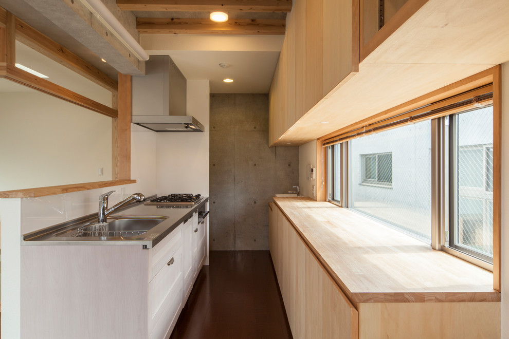 Aménagement d'une cuisine parallèle et encastrable asiatique en bois clair avec un évier intégré, un placard à porte plane, un plan de travail en inox, fenêtre, parquet foncé, un sol marron et un plan de travail gris.
