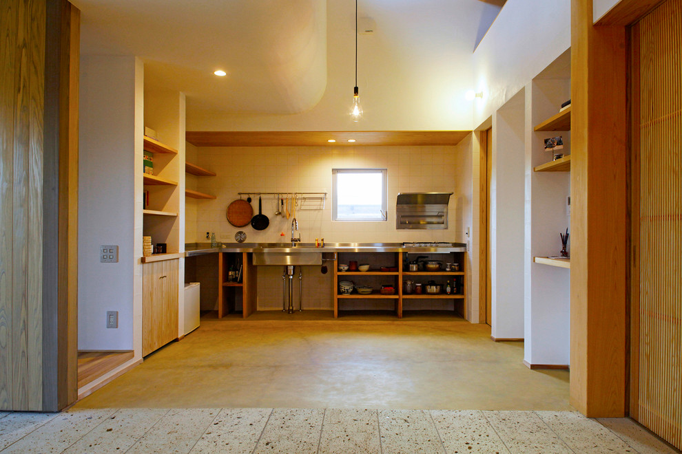 Diseño de cocina lineal de estilo zen abierta con fregadero integrado, armarios abiertos, encimera de acero inoxidable, salpicadero blanco, una isla y suelo marrón