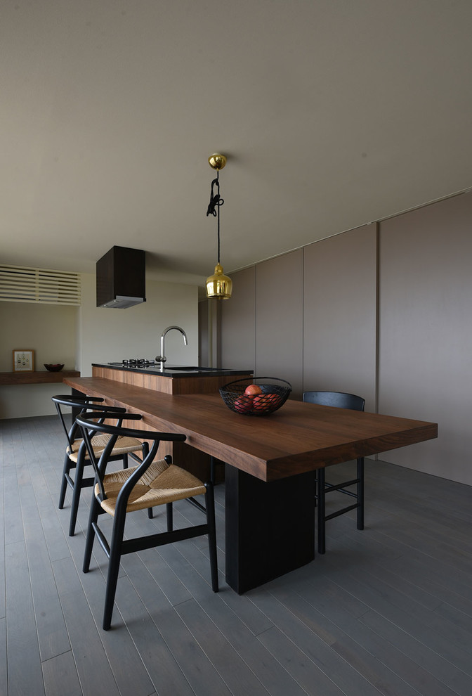 Photo of a medium sized modern single-wall kitchen/diner in Other with a submerged sink, flat-panel cabinets, dark wood cabinets, granite worktops, black appliances, medium hardwood flooring, an island, grey floors and black worktops.