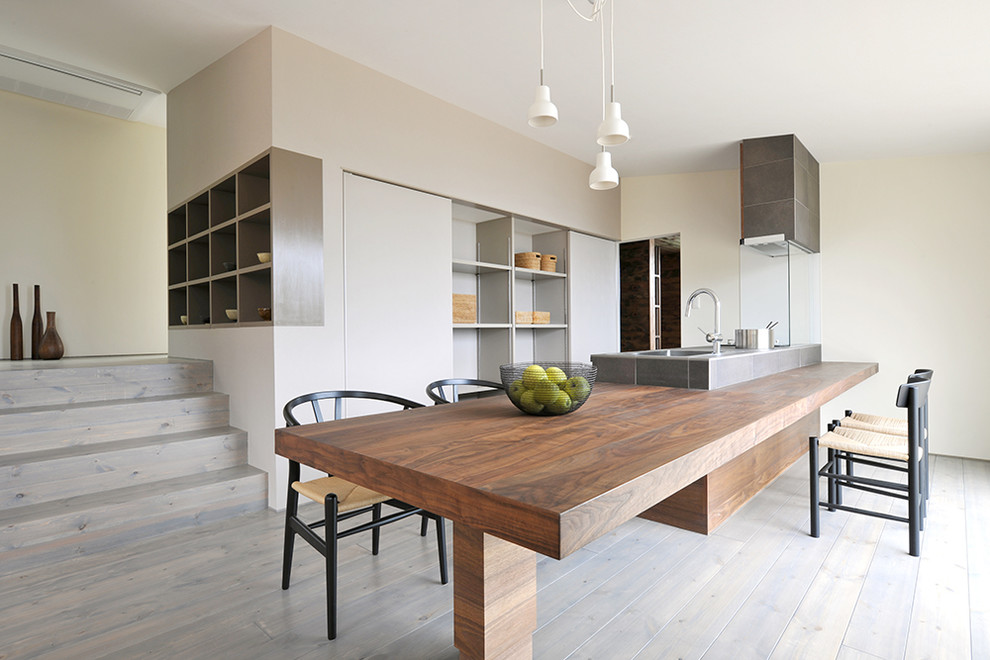 Inspiration for a large modern single-wall open plan kitchen in Other with a submerged sink, dark wood cabinets, tile countertops, white splashback, stainless steel appliances, light hardwood flooring, an island, grey floors and brown worktops.