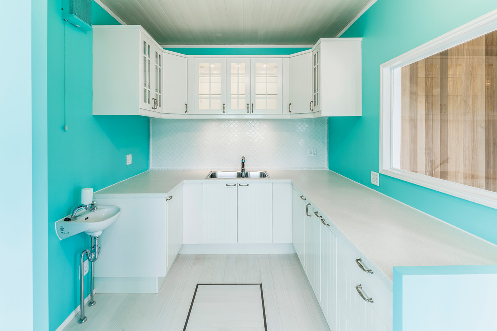 Inspiration for a coastal u-shaped painted wood floor enclosed kitchen remodel in Other with a double-bowl sink, white cabinets, flat-panel cabinets, white backsplash and white appliances