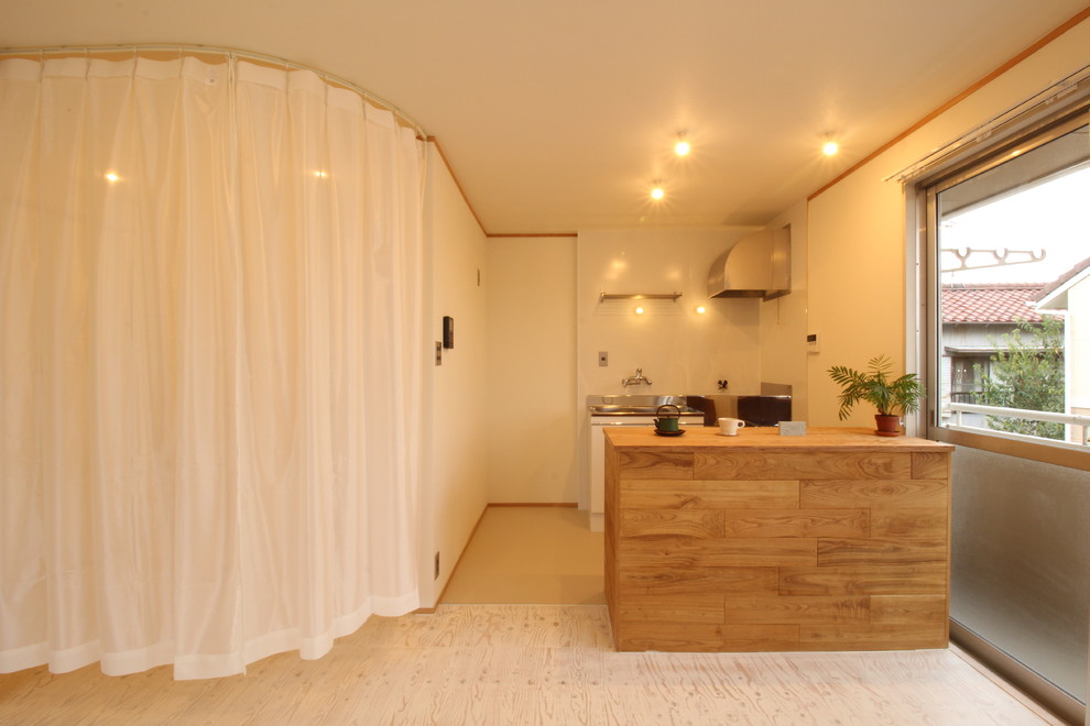 他の地域にある低価格のおしゃれなアイランドキッチン (木材カウンター、合板フローリング、白い床) の写真