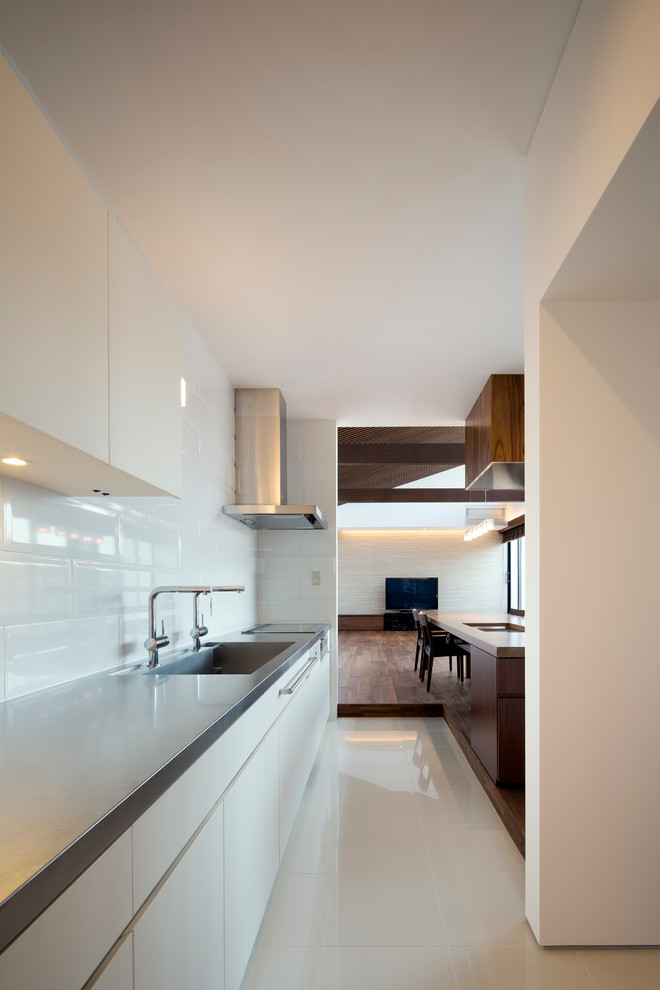 Einzeilige Moderne Küche mit integriertem Waschbecken, flächenbündigen Schrankfronten, weißen Schränken, Küchenrückwand in Weiß und Edelstahl-Arbeitsplatte in Kobe