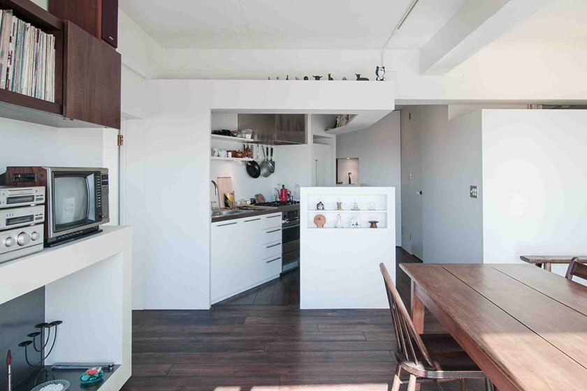 Modern inredning av ett litet kök, med en integrerad diskho, släta luckor, vita skåp, bänkskiva i rostfritt stål, vita vitvaror, mörkt trägolv och en köksö