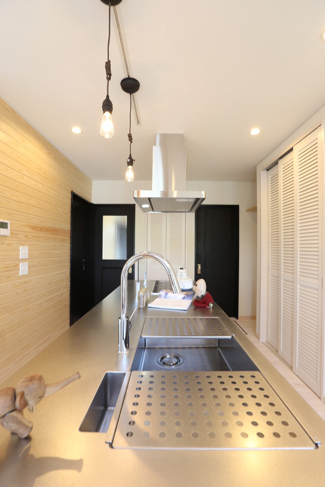 Foto på ett minimalistiskt linjärt kök med öppen planlösning, med en integrerad diskho, luckor med lamellpanel, vita skåp, bänkskiva i rostfritt stål, stänkskydd i trä, ljust trägolv och en köksö