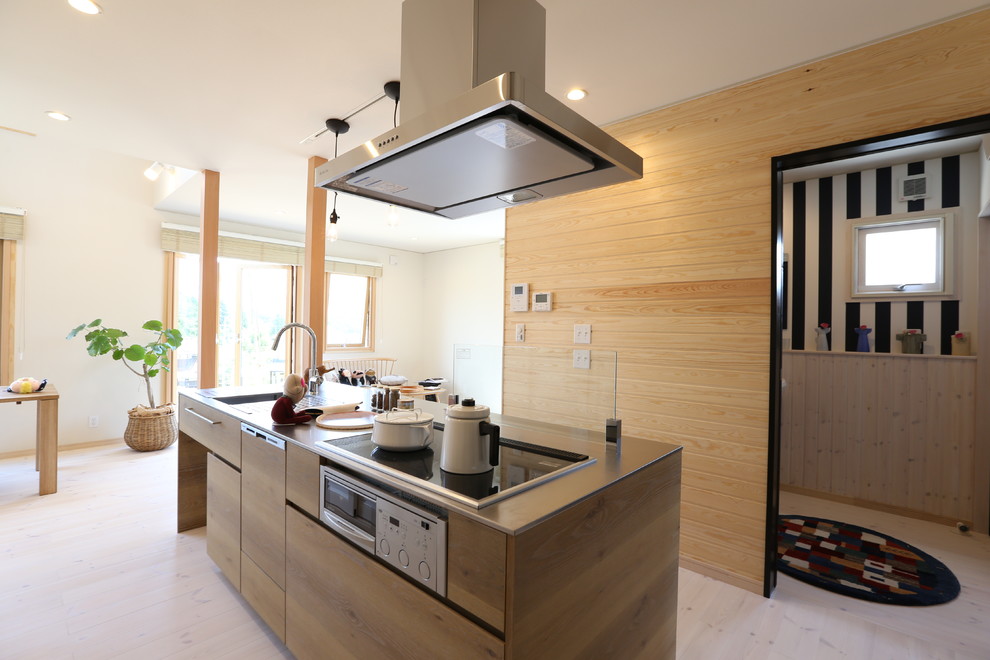 Inredning av ett minimalistiskt linjärt kök med öppen planlösning, med en integrerad diskho, vita skåp, bänkskiva i rostfritt stål, stänkskydd i trä, ljust trägolv, en köksö och släta luckor