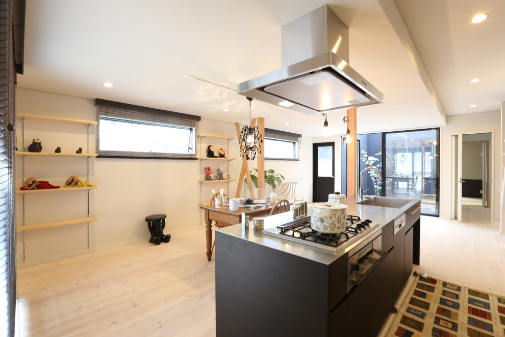 Пример оригинального дизайна: прямая кухня-гостиная в восточном стиле с монолитной мойкой, столешницей из нержавеющей стали, островом, плоскими фасадами, черными фасадами, деревянным полом и бежевым полом