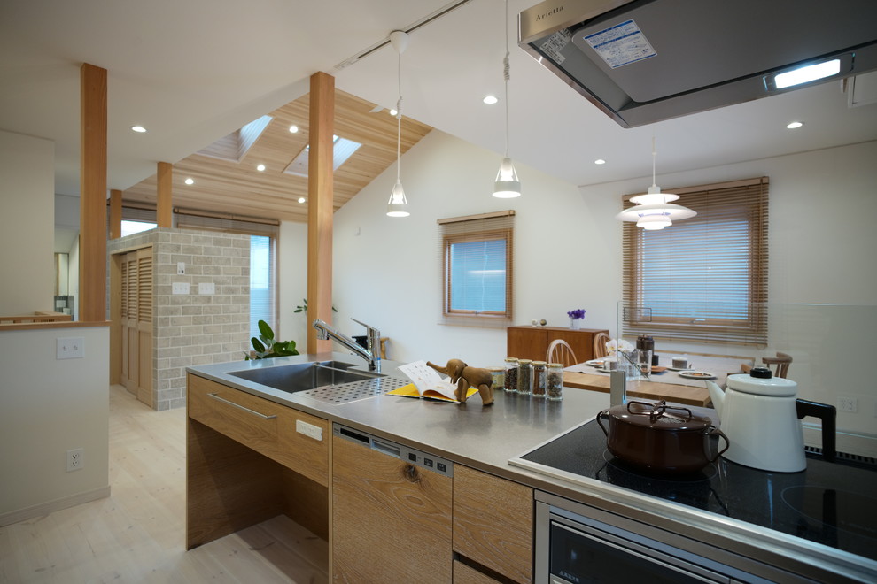 Inredning av ett skandinaviskt linjärt kök med öppen planlösning, med en integrerad diskho, luckor med profilerade fronter, skåp i mellenmörkt trä, bänkskiva i rostfritt stål, beige stänkskydd, stänkskydd i trä, ljust trägolv, en köksö och vitt golv