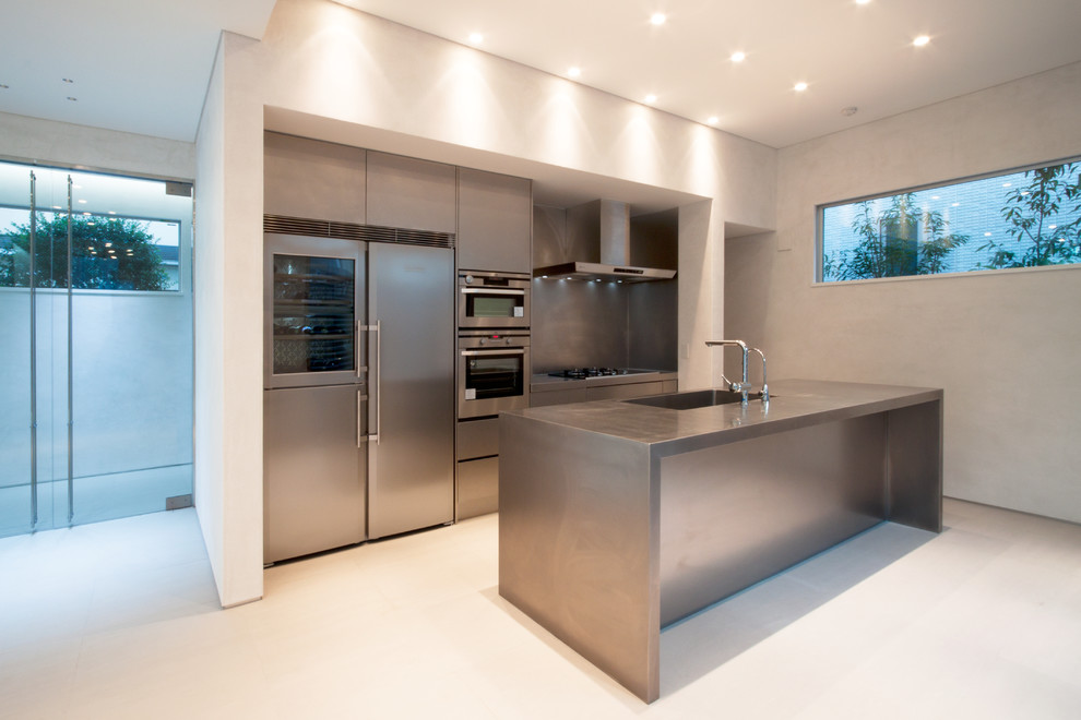 Diseño de cocina moderna con fregadero integrado, armarios con paneles lisos, puertas de armario en acero inoxidable, encimera de acero inoxidable, una isla y suelo blanco