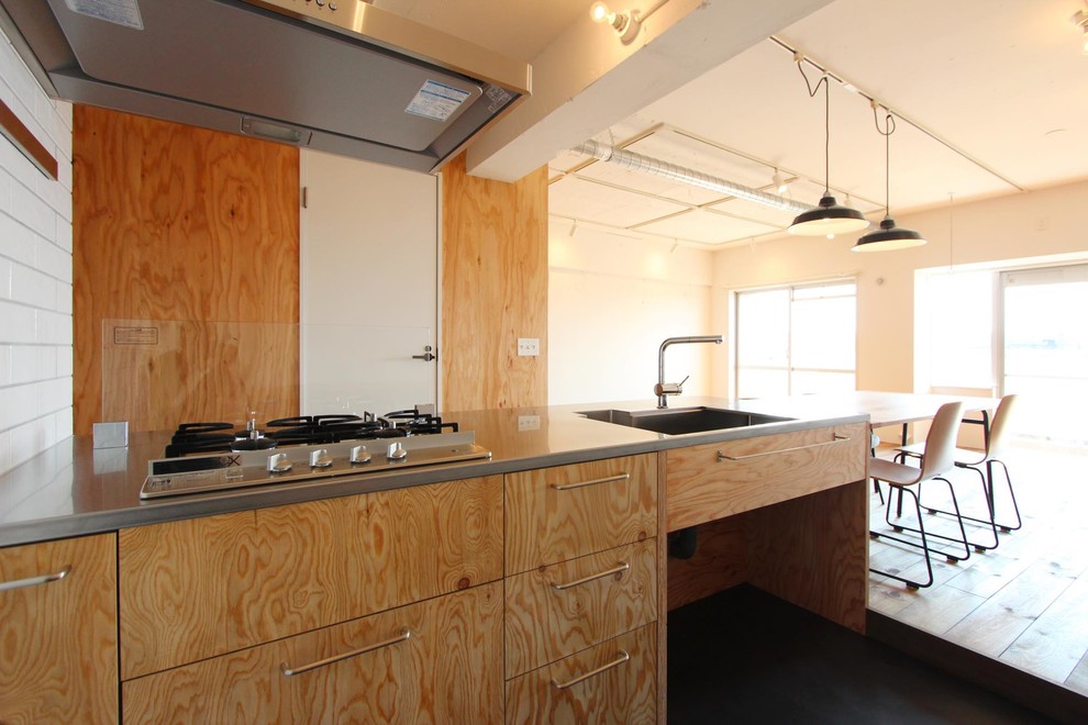 東京23区にあるインダストリアルスタイルのおしゃれなキッチン (一体型シンク、フラットパネル扉のキャビネット、淡色木目調キャビネット、ステンレスカウンター、ガラス板のキッチンパネル、シルバーの調理設備) の写真