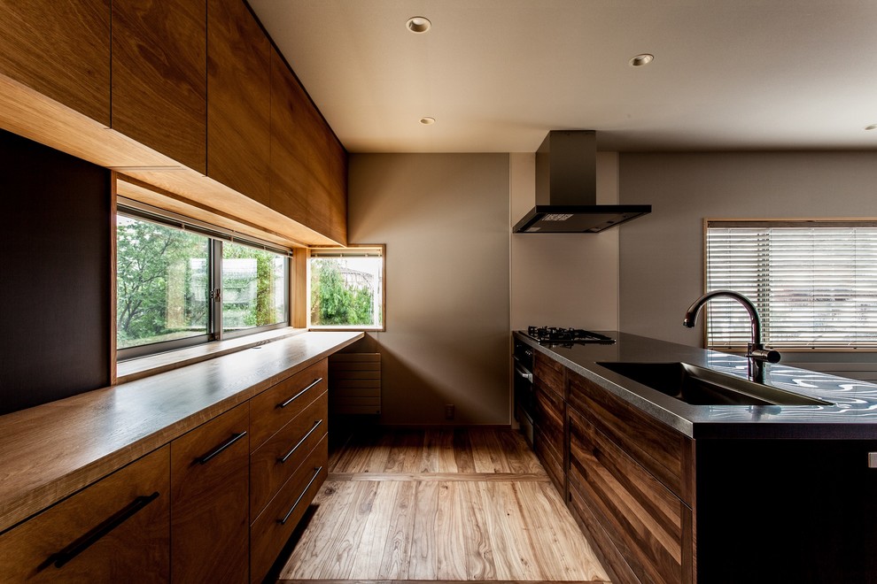 Modern inredning av ett mellanstort kök med öppen planlösning, med en integrerad diskho, skåp i mörkt trä, bänkskiva i rostfritt stål, stänkskydd i trä, svarta vitvaror, mellanmörkt trägolv och en halv köksö