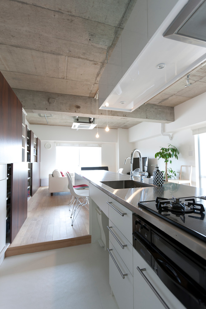 Foto på ett mellanstort funkis linjärt kök med öppen planlösning, med en integrerad diskho, släta luckor, vita skåp, bänkskiva i rostfritt stål, vitt stänkskydd, rostfria vitvaror och mellanmörkt trägolv