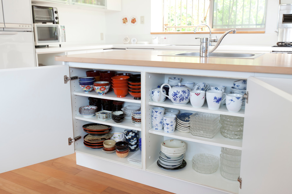 Inredning av ett modernt mellanstort kök, med en undermonterad diskho, luckor med glaspanel, vita skåp, träbänkskiva, vitt stänkskydd, stänkskydd i keramik, integrerade vitvaror, mellanmörkt trägolv och en halv köksö