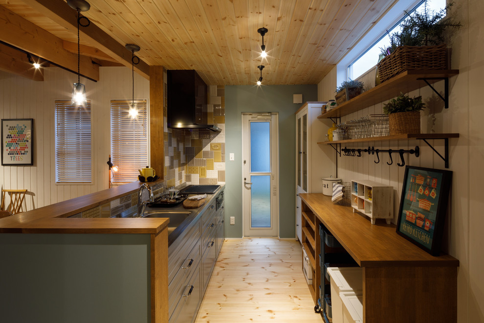 他の地域にある北欧スタイルのおしゃれなキッチン (シングルシンク、落し込みパネル扉のキャビネット、グレーのキャビネット、ステンレスカウンター、淡色無垢フローリング、ベージュの床、茶色いキッチンカウンター) の写真