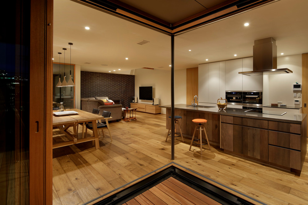 Open concept kitchen - large asian galley medium tone wood floor and brown floor open concept kitchen idea in Tokyo with an undermount sink, flat-panel cabinets, distressed cabinets, quartz countertops, black appliances, an island and black countertops