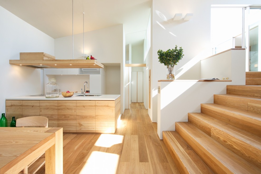 Scandi single-wall open plan kitchen in Osaka with flat-panel cabinets, light wood cabinets, light hardwood flooring, composite countertops, white splashback, wood splashback, a breakfast bar and white worktops.