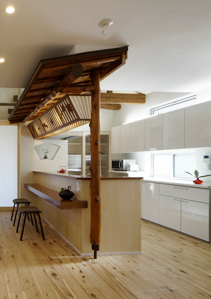 Ejemplo de cocina de estilo zen de tamaño medio abierta con armarios con paneles lisos, puertas de armario blancas, suelo de madera clara, península y barras de cocina