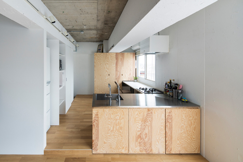 Diseño de cocina minimalista con armarios con paneles lisos, puertas de armario blancas, encimera de acero inoxidable, salpicadero blanco, suelo de madera en tonos medios, península y suelo marrón