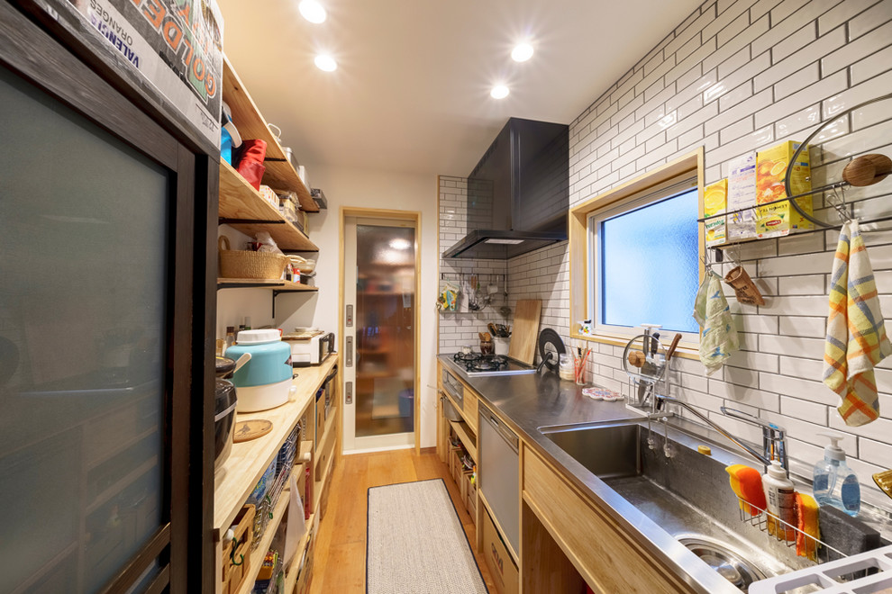 Idéer för ett avskilt, litet modernt linjärt kök, med en integrerad diskho, öppna hyllor, skåp i ljust trä, bänkskiva i rostfritt stål, vitt stänkskydd, stänkskydd i tunnelbanekakel, rostfria vitvaror, plywoodgolv, en köksö och brunt golv