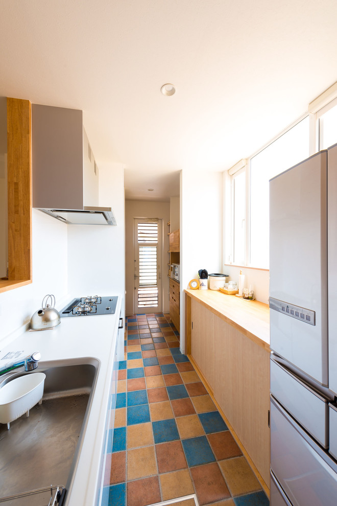 Photo of a mediterranean single-wall kitchen in Other with a single-bowl sink, flat-panel cabinets, white cabinets, white splashback, ceramic flooring, a breakfast bar, multi-coloured floors and brown worktops.