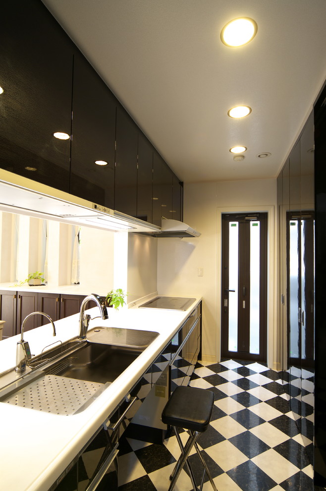 На фото: прямая кухня в современном стиле с одинарной мойкой, плоскими фасадами, черными фасадами, полуостровом, разноцветным полом и белой столешницей