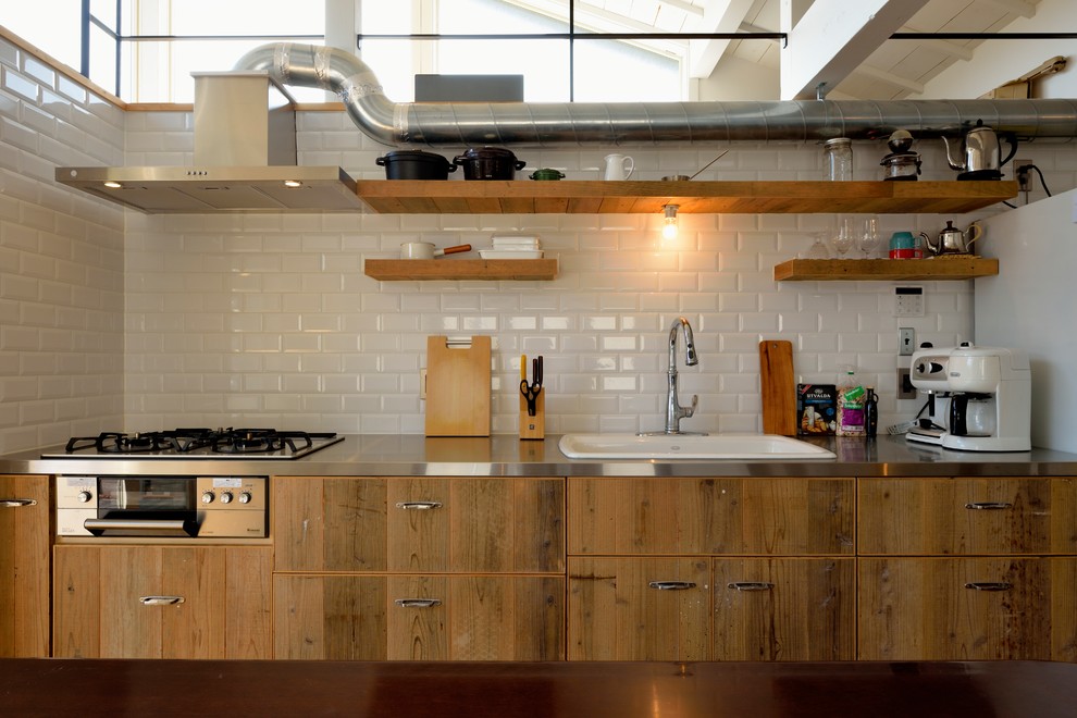 Aménagement d'une cuisine industrielle en bois brun avec un évier posé, un placard à porte plane, un plan de travail en inox et une crédence blanche.