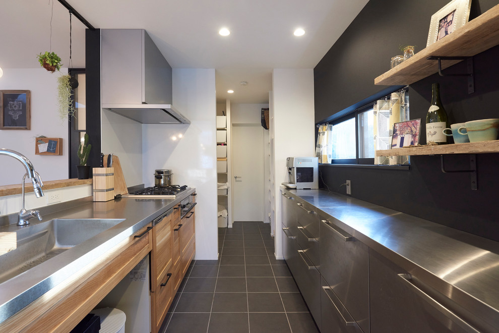 Idéer för att renovera ett industriellt linjärt kök med öppen planlösning, med en enkel diskho, luckor med infälld panel, skåp i mellenmörkt trä, bänkskiva i rostfritt stål, en halv köksö och svart golv