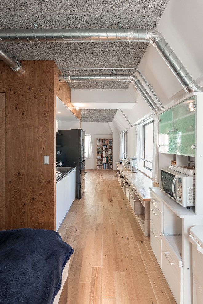 Bild på ett litet industriellt linjärt kök med öppen planlösning, med en integrerad diskho, släta luckor, vita skåp, bänkskiva i rostfritt stål, vitt stänkskydd, stänkskydd i skiffer, vita vitvaror, plywoodgolv och brunt golv