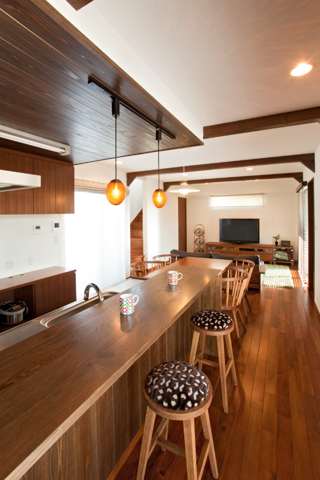 На фото: параллельная кухня в восточном стиле с одинарной мойкой, столешницей из нержавеющей стали, паркетным полом среднего тона, островом и коричневым полом с