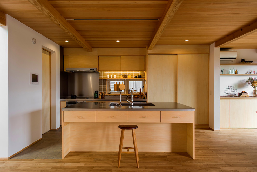 Asiatisk inredning av ett brun brunt kök, med en integrerad diskho, släta luckor, skåp i ljust trä, bänkskiva i rostfritt stål, mellanmörkt trägolv, en köksö och brunt golv