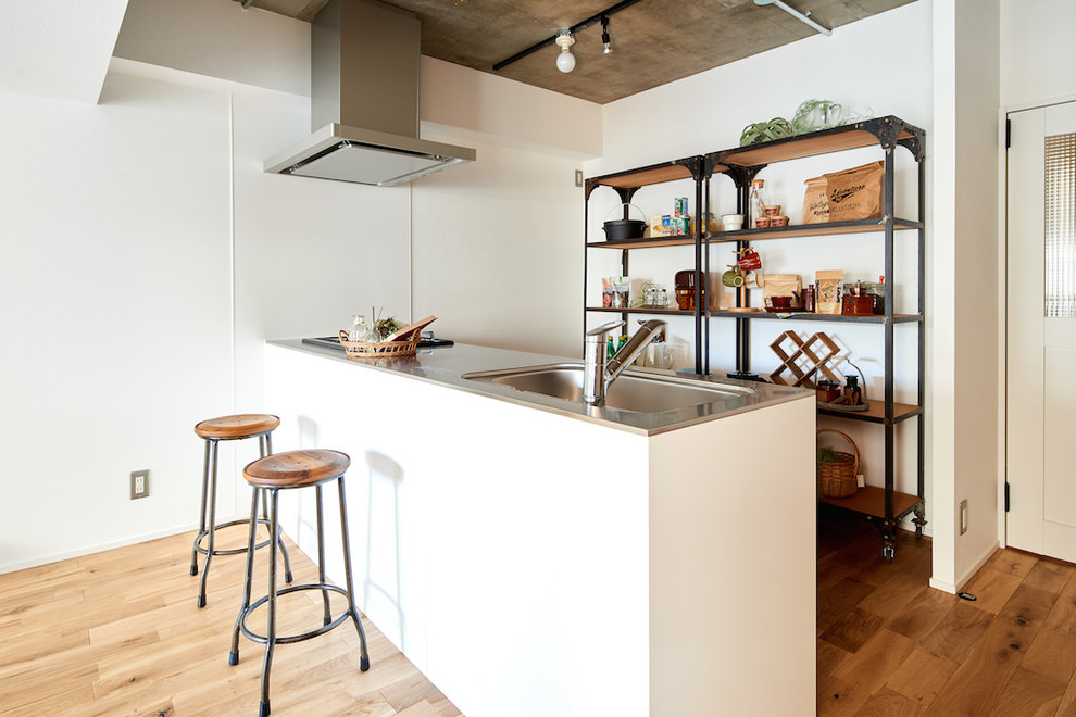 他の地域にあるコンテンポラリースタイルのおしゃれなキッチン (ステンレスカウンター、無垢フローリング、アンダーカウンターシンク、茶色い床、グレーのキッチンカウンター) の写真