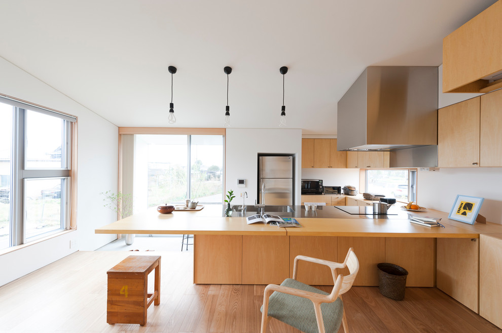 Modern inredning av ett kök, med en integrerad diskho, skåp i mellenmörkt trä, bänkskiva i rostfritt stål, rostfria vitvaror, betonggolv, en köksö och brunt golv
