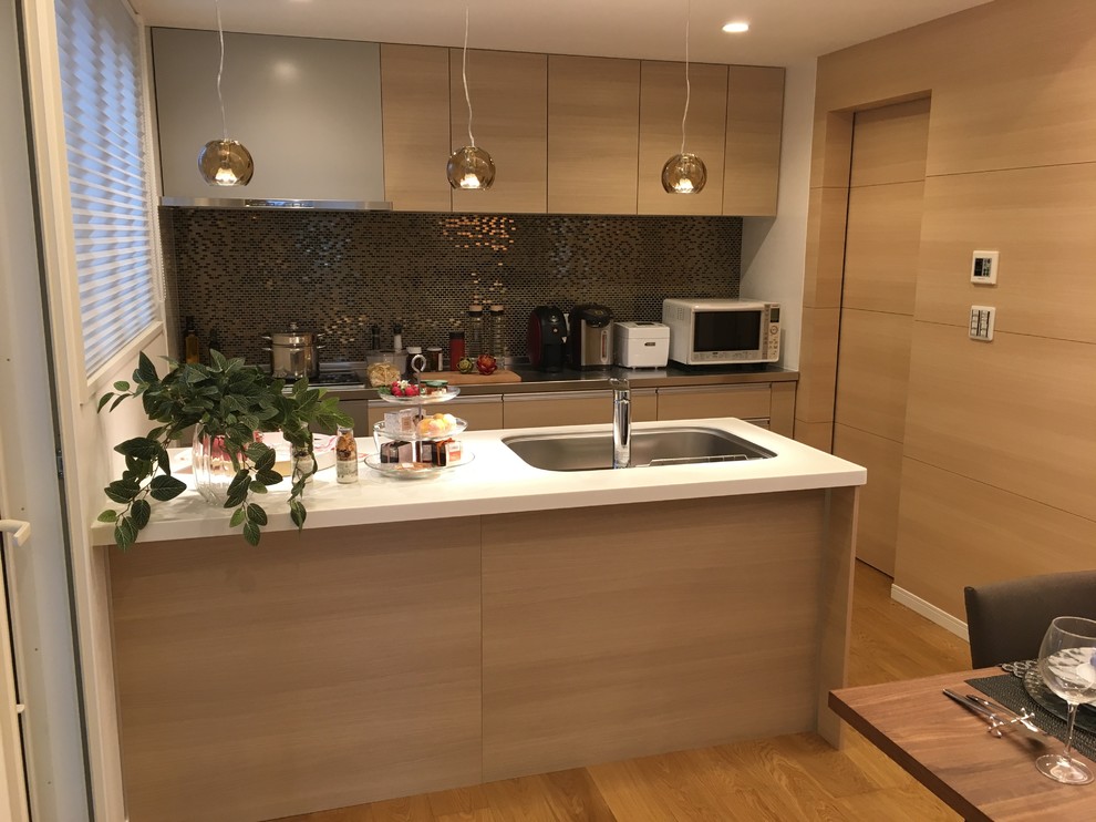 Cette image montre une cuisine ouverte parallèle minimaliste avec un évier encastré, un plan de travail en surface solide, une crédence beige, une crédence en mosaïque, un électroménager en acier inoxydable, un sol en contreplaqué, îlot et un sol beige.
