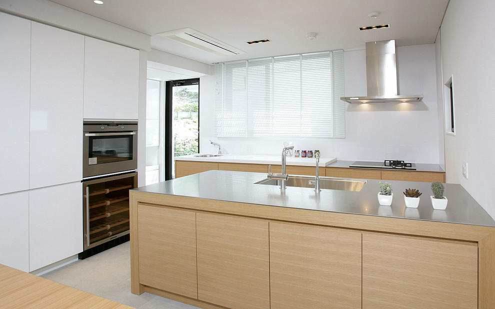 Foto di una cucina parallela minimal con lavello integrato, ante in legno chiaro, top in acciaio inossidabile, paraspruzzi bianco, elettrodomestici in acciaio inossidabile e penisola