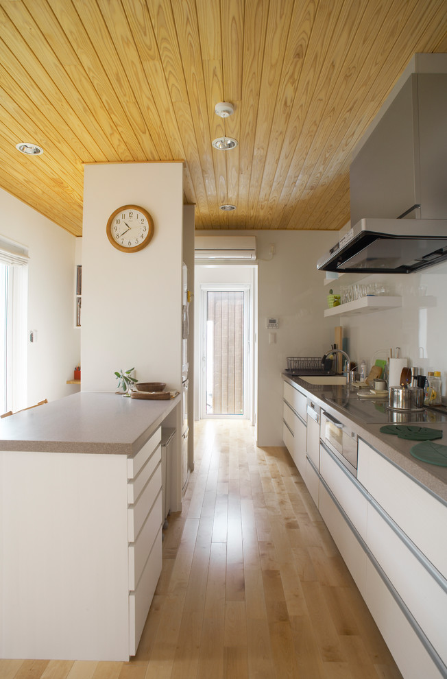 This is an example of a world-inspired galley kitchen in Other with a single-bowl sink, flat-panel cabinets, white cabinets, light hardwood flooring, an island and brown floors.