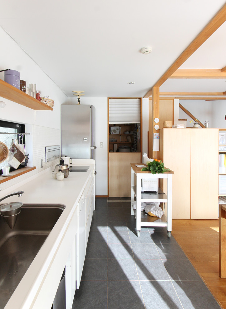 На фото: прямая кухня-гостиная в восточном стиле с одинарной мойкой, плоскими фасадами, белыми фасадами, белым фартуком, полуостровом и серым полом