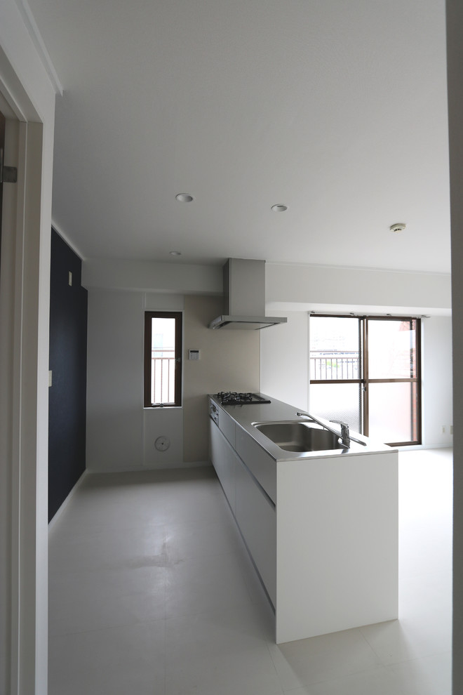 Inspiration för mellanstora moderna linjära kök med öppen planlösning, med en integrerad diskho, släta luckor, vita skåp, bänkskiva i rostfritt stål, vitt stänkskydd, stänkskydd i cementkakel, rostfria vitvaror, vinylgolv, en köksö och vitt golv