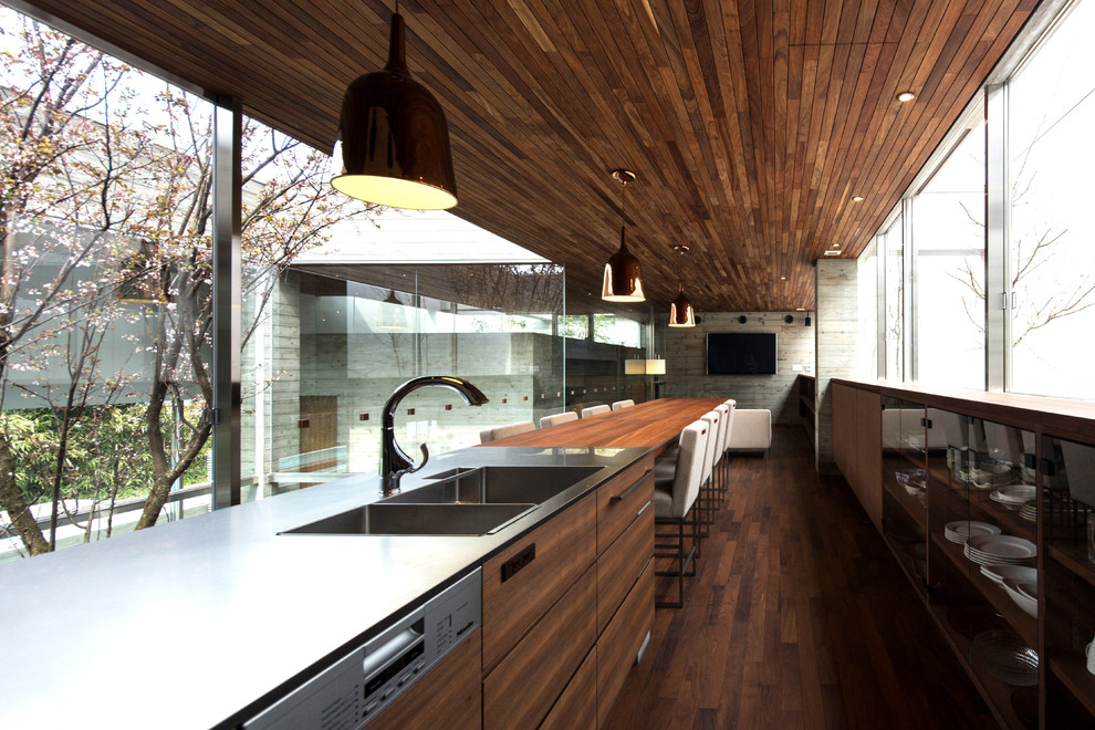 Foto på ett funkis kök, med en dubbel diskho, släta luckor, skåp i mellenmörkt trä, bänkskiva i rostfritt stål, rostfria vitvaror och mörkt trägolv