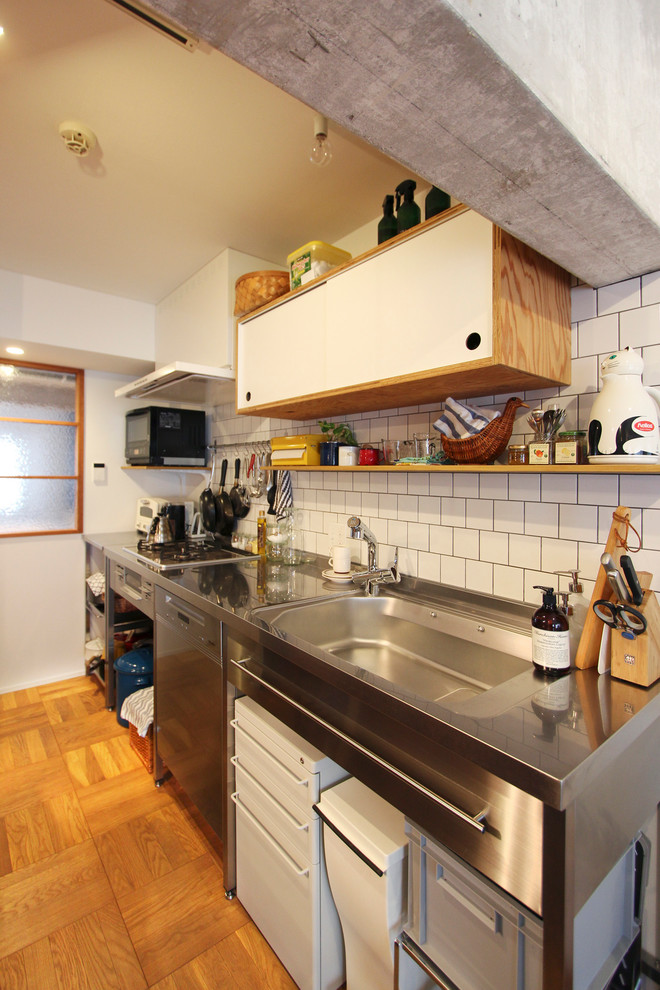 東京23区にあるアジアンスタイルのおしゃれなキッチン (シングルシンク、ステンレスカウンター、白いキッチンパネル、サブウェイタイルのキッチンパネル、無垢フローリング、茶色い床) の写真
